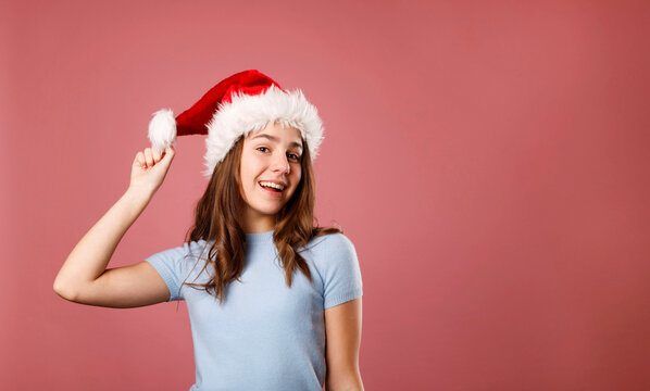 Young happy teenager girl wearing Santa Claus red hat over pink background. Christmas and New Year celebration concept.
