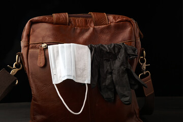 Men's leather bag in orange color. A medical mask and protective gloves stick out of the pocket. Dark background.