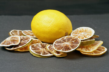 Ripe lemon surrounded by dried citrus slices on a dark background.