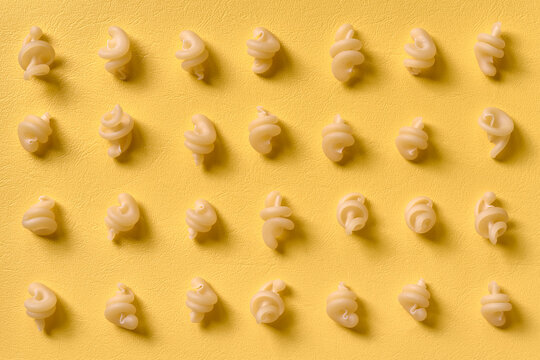 Rows of whole raw funghetto pasta flat on a yellow background