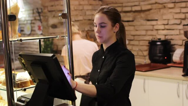 a girl in black clothes standing at the cash register in the morning, customer service in a cafe.