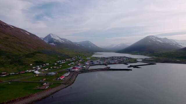 Wide aerial turning shot of coastal town below snow covered mountains. Shot in Iceland.