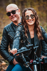 Fototapeta premium Cute couple near a red motorcycle in the autumn forest. Relationship concept. A pair of bikers in leather jackets.