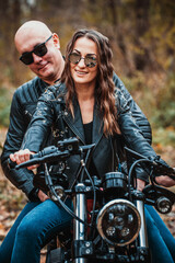 Plakat Cute couple near a red motorcycle in the autumn forest. Relationship concept. A pair of bikers in leather jackets.