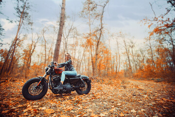 woman in a leather jacket on a motorcycle in nature. biker on a motorcycle in the autumn forest