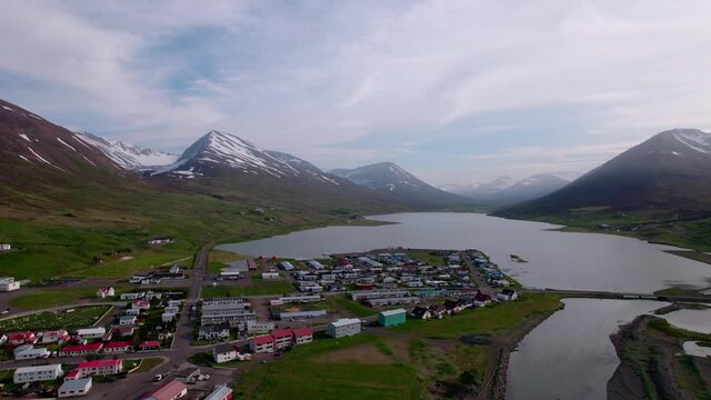 Aerial flying over small town with snow covered mountains in the distance. Fjord in Iceland.