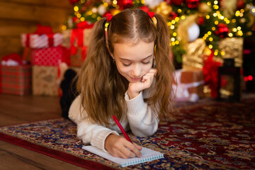 Fototapeta premium A child's letter to Santa on the eve of a Happy New Year. Template, blank, postcard. A cute girl who writes a letter to Santa near a beautiful Christmas tree