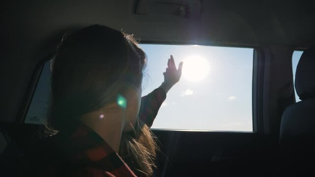 Summer travel.beautiful girl travels by car. kid girl stuck her hand out of car window towards sun. kid opens window to get some fresh air, hand moves in wind. hand glares sun, driving car fast.