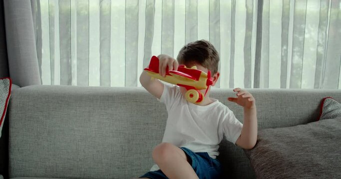 A cute little preschooler boy playing at home on the sofa with a toy airplane, a cute little son child sitting on the sofa launches an airplane in his hands.