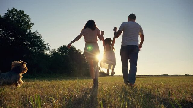 Happy family walks in park in sunshine. Mom, dad and kid are happy. girl holds hands of her parents. Parents hold their kid hands at sunset. Happiness concept. Family together.