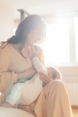 Happy mom breastfeeding her baby in the bedroom - obrazy, fototapety, plakaty
