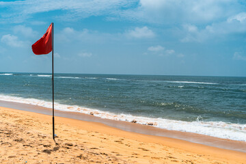Fototapeta na wymiar Czerwona flaga na tropikalnej plaży, widok na ocean.