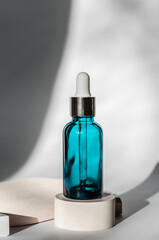 Turquoise cosmetic bottle with a dropper on a beige podium with beautiful shadows. Skin Care Cosmetics