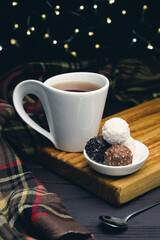 White cup of tea with spoon and chocolate candy on blurred background with christmas lights