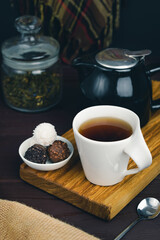 White cup of black tea with spoon and candy on wooden desk. Sweet dessert with tea concept