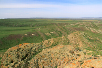 Green valley of the Malaysary ridge, in the foreground there are red rocks, distant view of the valley plateau, sky with clouds, summer, sunny