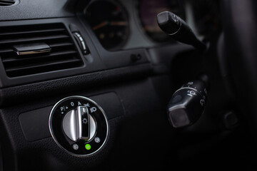 An unrecognizable male driver activates lights or turn signals on the control lever behind the steering wheel of the car.