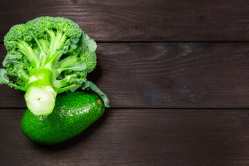 Fresh broccoli and avocado fruit on a dark wooden background with space for text. Top view. Concept of healthy, vegetarian, diet food.
