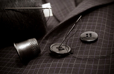 A needle and thread sews up a button on a plaid suit. Thimble. Textile