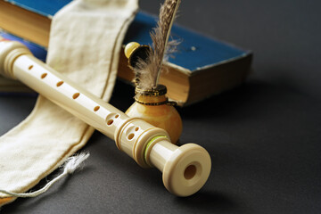 A plastic recorder lies on a dark background next to books and an inkwell with a pen