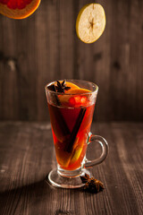 christmas mulled wine, in a transparent glass with fruit on a dark wooden background surrounded by flying spices and fruits