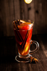 christmas mulled wine, in a transparent glass with fruit on a dark wooden background surrounded by flying spices and fruits