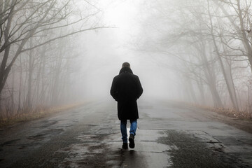 Fog landscape. Man walking  alone on scary foggy misty road.