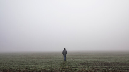 Fototapeta na wymiar Lonly man walk away into the misty foggy road in a dramatic mystic scene. Guy walking in a foggy autumn landscape