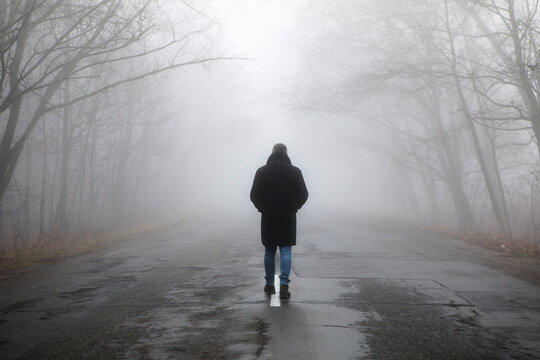 Fog landscape. Man walking  alone on scary foggy misty road.