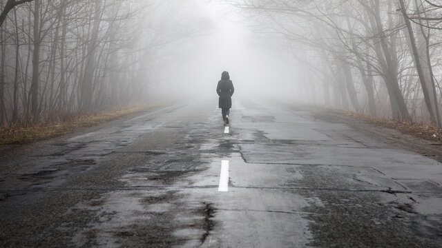 Lonly woman  walk away into the misty foggy road in a dramatic mystic scene.