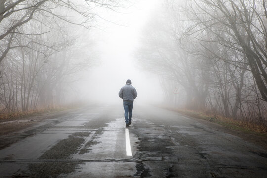 Lonly man  walk away into the misty foggy road in a dramatic mystic scene. Guy walking in a foggy autumn landscape