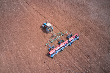 Tractor with a trailed seeder in the field. There are two farmers on the seeder who monitor the process of sowing seeds and fertilizing from the hopper. Shooting from a drone.