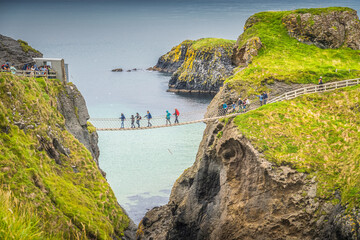 Closeup on people on the Carrick a Rede rope bridge and scenic island surrounded by turquoise...