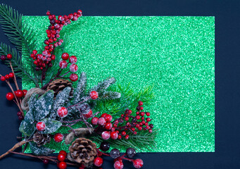 Spruce branch with red berries on a green, shiny background. Christmas background.