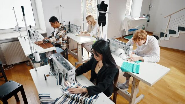 Dressmaking process. Group of young diverse dressmakers working on sewing machines, creating fashion collection