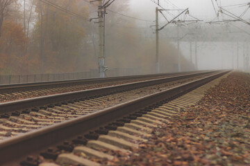 Fototapeta na wymiar A railroad going into fog in the middle of an autumn landscape. Rails lost in the distance and disappearing into the fog.