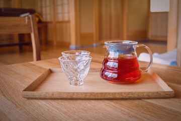Soft focused elegant glass tea cups and teapot with rooibos herbal tea on traditional japanese wooden kotatsu table on blurred minimalist background in hot springs spa health club.Wellness recreation
