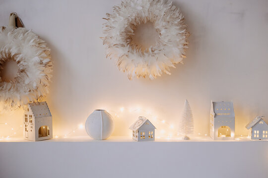 Christmas Wreath Decoration and Garland Copy Space Photo. Houses and Fir-tree Toys, Glowing Lamps and Fashion Accessories Made from Bird Feathers on Wall. New Year Traditional Design Ornament
