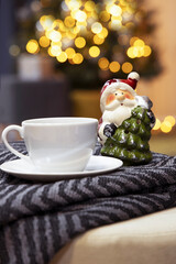 A cup of tea and a figure of Santa Claus on the background of a Christmas tree, a blurred background with garland lights