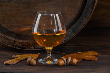 Glass with whiskey, brandy on a vintage background of a rustic oaken barrel. Alcoholic beverage. Still life in the old style