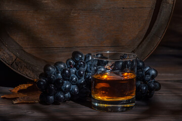 Glass with cognac, brandy on a vintage background of a rustic oaken barrel. Alcoholic beverage. Still life in the old style - obrazy, fototapety, plakaty
