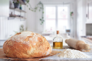 freshly baked artisan bread in baking paper on table with ingredients and rolling pin with kitchen background