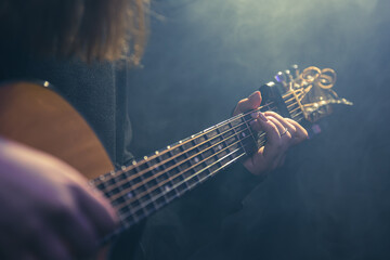 Young woman playing acoustic guitar in a dark room with haze.
