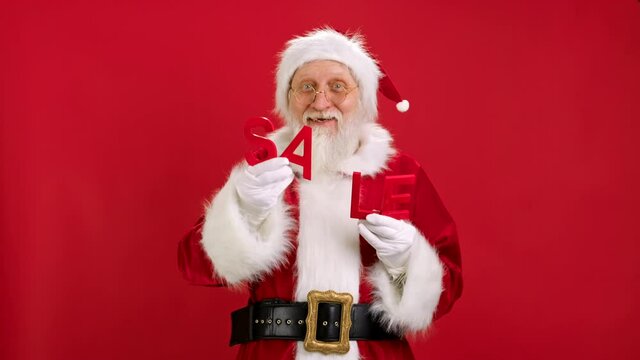 Cheerful Santa Claus is Happy With Big Discounts at Christmas Black Friday Dancing Holding Red Letters With Word SALE on Red Studio Background. Discount sale, Black Friday, Cyber Monday.