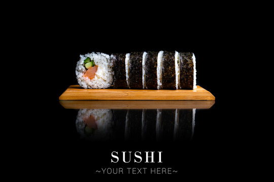 Japanese Maki sushi roll with salmon and cucumber. Served on wooden board. Asian dish on black background with reflection. Banner with Text space 
