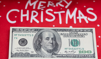 US 100 dollar banknote and Merry Christmas text on red background