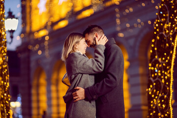 Christmas people cuddling and hugging outdoors on New Year. A happy couple in love standing on the street on Christmas, cuddling, and hugging.