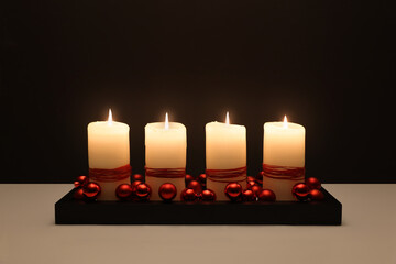 Vier brennende weiße Kerzen vor schwarzem Hintergrund im Advent