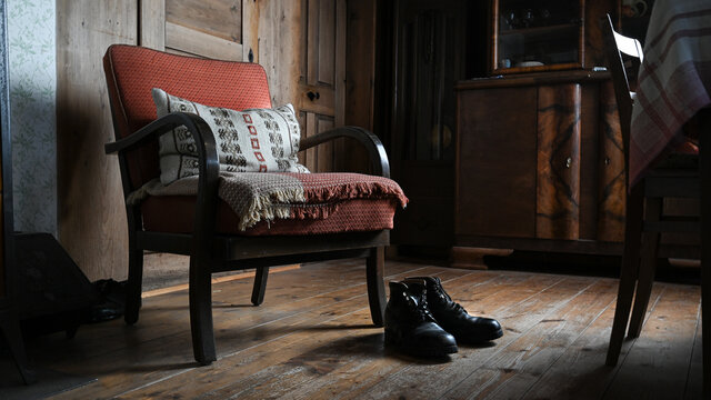 Alter Sessel mit Kissen und alten Schuhen in alter Bauernstube mit Holzboden im Haus auf Bauernhof in Europa.