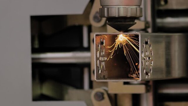 Automatic cnc laser cutting machine working with metal square pipe with many sparks at factory, plant - close up, slow motion. Metalworking, industrial, manufacturing, technology and equipment concept